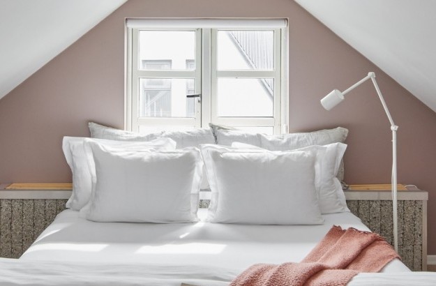 Cozy attic-style bedroom with slanted ceiling, soft bedding and pastel walls at Thingholt apartments from Center Hotels in Reykjavik.
