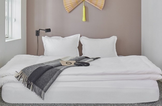 Neatly made double bed with bedside lighting in a cozy setting at Thingholt apartments from Center Hotels.