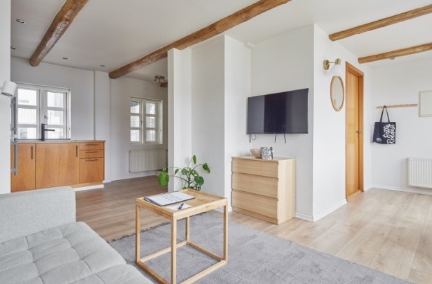 Bright living room with exposed wooden beams, a wall-mounted TV, modern furniture and neatural tones.