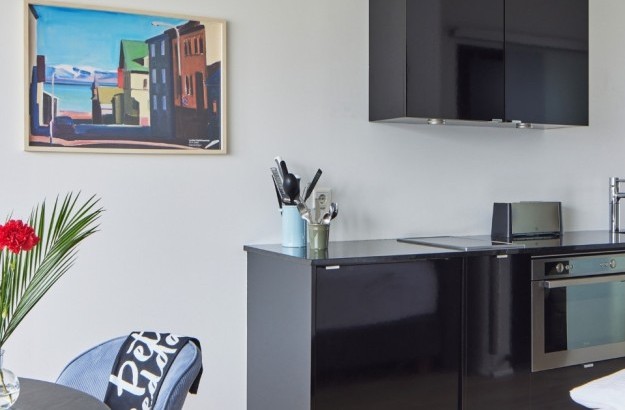 Compact kitchenette with modern appliances and colorful wall art in studio aprtment at Thingholt Apartments from Center Hotels in Reykjavik.