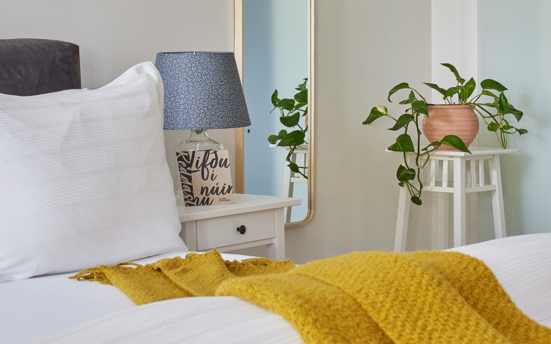 Detail of bedside table with lamp, pillow, and indoor plant in the family apartment at Thingholt apartments from Center Hotels in Reykjavik.