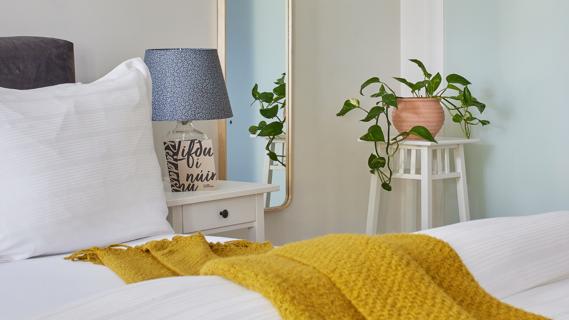 Detail of bedside table with lamp, pillow, and indoor plant in the family apartment at Thingholt apartments from Center Hotels in Reykjavik.