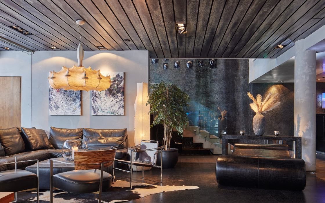 Stylish lounge at Thingholt by Center Hotels with black leather sofa, contemporary pendant lighting, abstract art, indoor plants, and a staircase with glass panels leading upward.