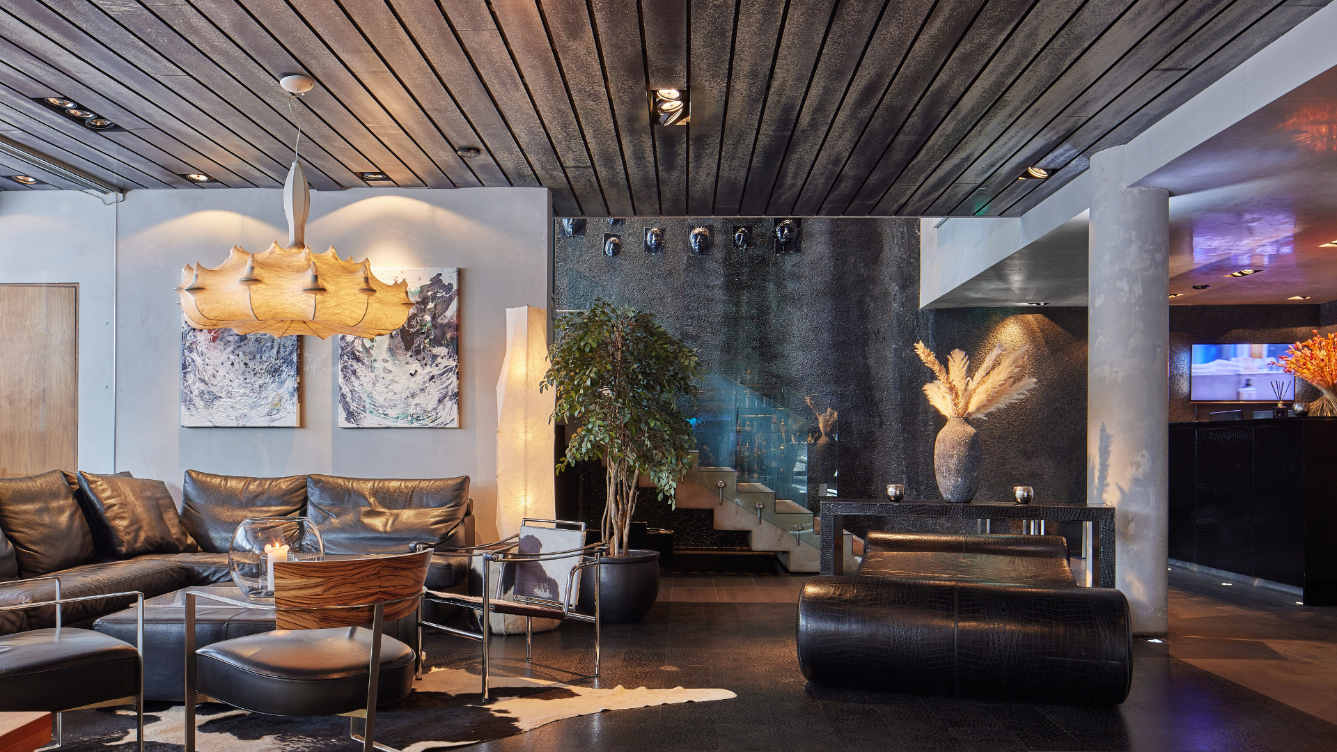 Stylish lounge at Thingholt by Center Hotels with black leather sofa, contemporary pendant lighting, abstract art, indoor plants, and a staircase with glass panels leading upward.