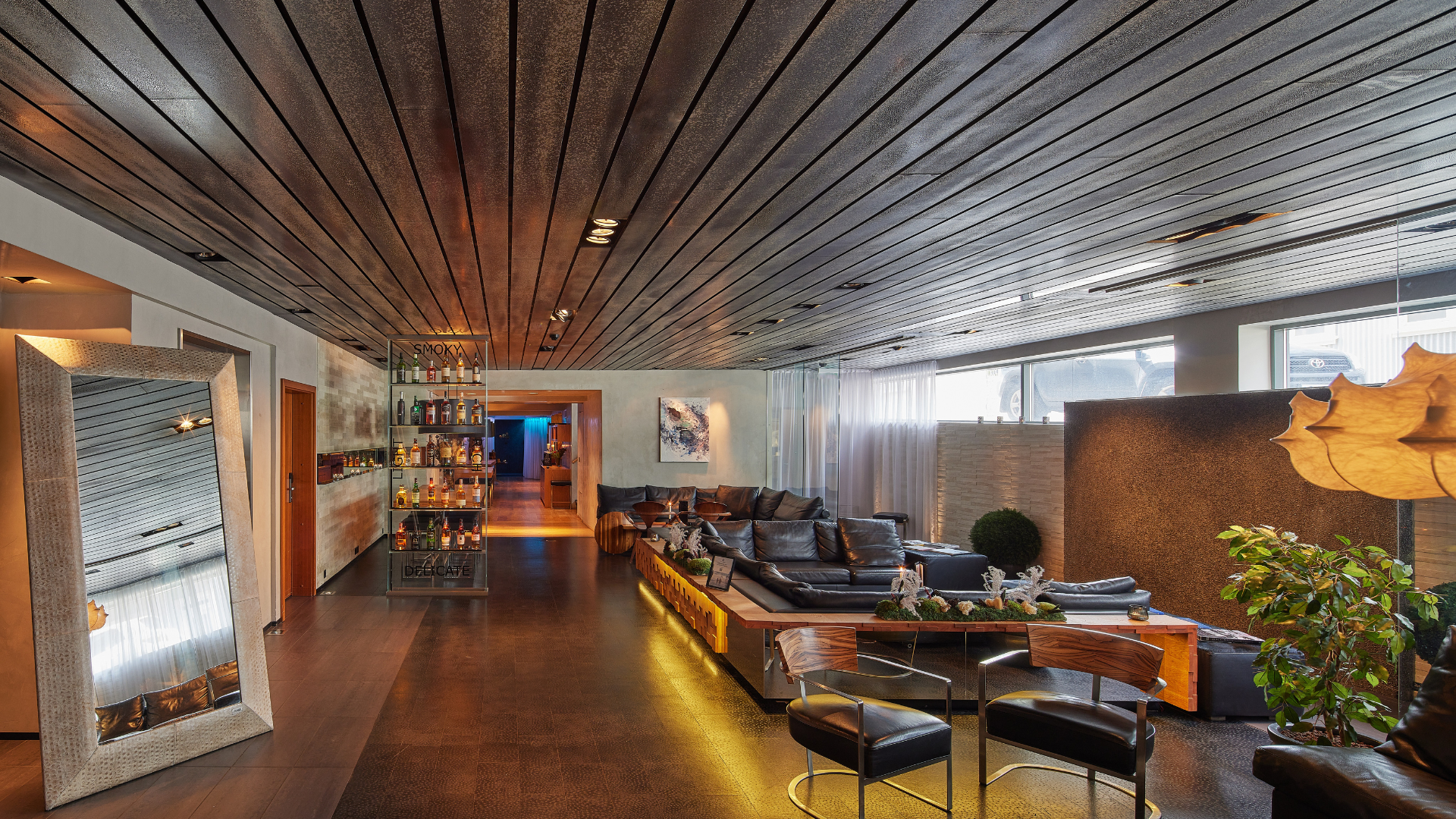 Lobby lounge at Thingholt by Center Hotels showing a tall decorative mirror, cozy lounge area with leather sofas, designer lighting, bar shelves with spirits, and natural daylight filtering t