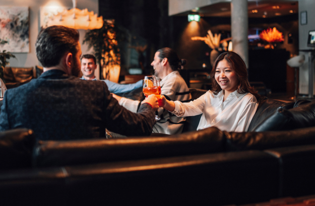  Group of guests enjoying cocktails in the lounge at Thingholt by Center Hotels, seated on black leather sofas surrounded by soft lighting and plants.