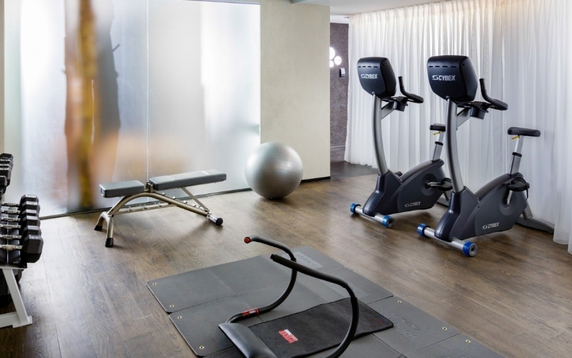 Fitness room at Thingholt by Center Hotels in Reykjavík featuring upright exercise bikes, dumbbell rack, weight bench, exercise mat with ab roller, and a stability ball in a softly lit space
