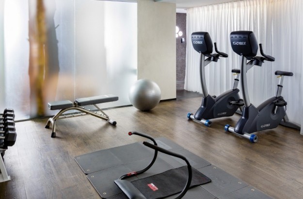 Fitness room at Thingholt by Center Hotels in Reykjavík featuring upright exercise bikes, dumbbell rack, weight bench, exercise mat with ab roller, and a stability ball in a softly lit space