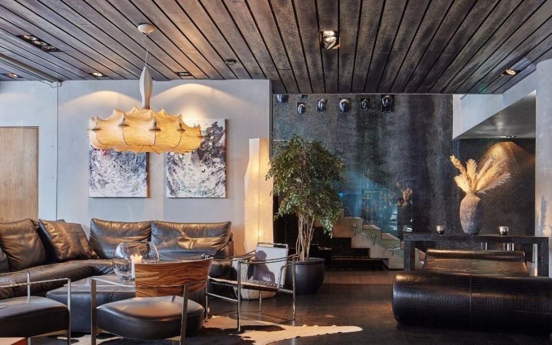 Stylish lounge at Thingholt by Center Hotels with black leather sofa, contemporary pendant lighting, abstract art, indoor plants, and a staircase with glass panels leading upward.
