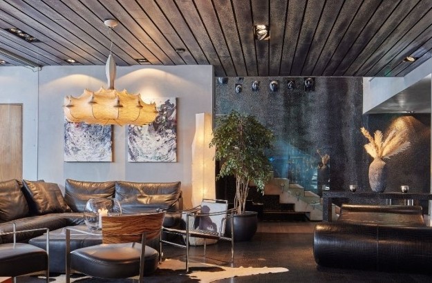 Stylish lounge at Thingholt by Center Hotels with black leather sofa, contemporary pendant lighting, abstract art, indoor plants, and a staircase with glass panels leading upward.