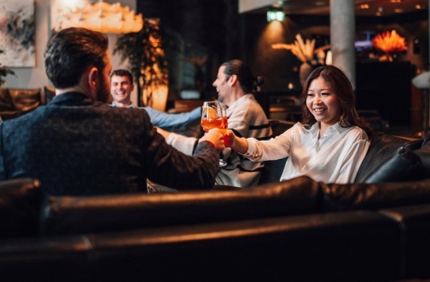 Group of guests enjoying cocktails in the lounge at Thingholt by Center Hotels, seated on black leather sofas surrounded by soft lighting and plants.