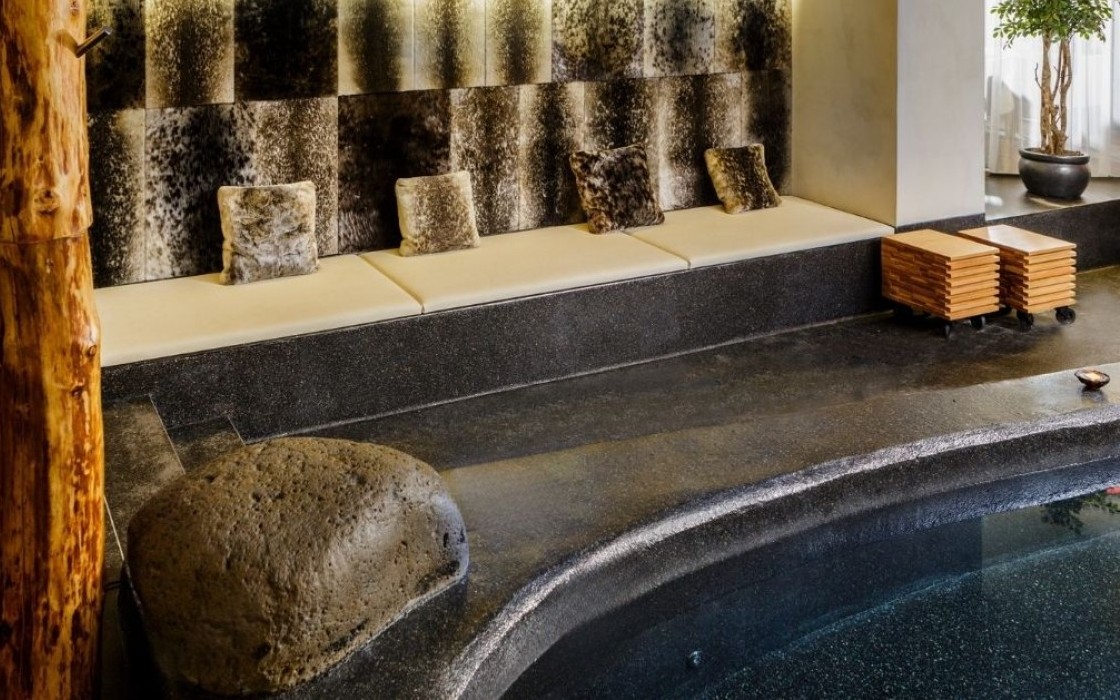Spa lounge seating at Isafold spa in Reykjavik, located inside Thingholt by Center Hotels, featuring a long cushioned bench with faux-fur pillows, natural wood accents, lava rocks, and ambien