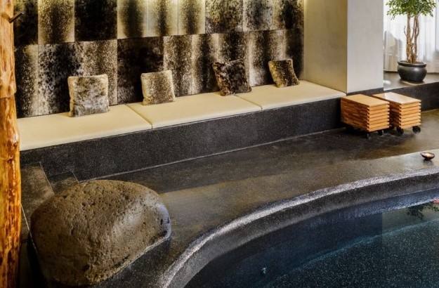 Spa lounge seating at Isafold spa in Reykjavik, located inside Thingholt by Center Hotels, featuring a long cushioned bench with faux-fur pillows, natural wood accents, lava rocks, and ambien