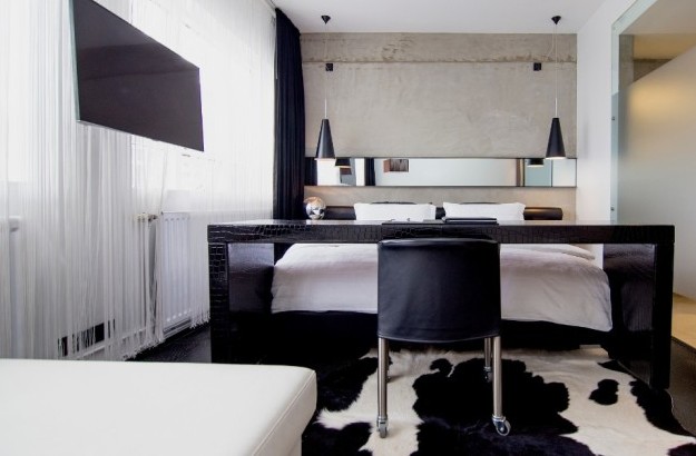 Modern Deluxe Room at Thingholt by Center Hotels in Reykjavík featuring a large double bed, concrete accent wall, black crocodile-textured desk, pendant lighting, and frosted glass partitions