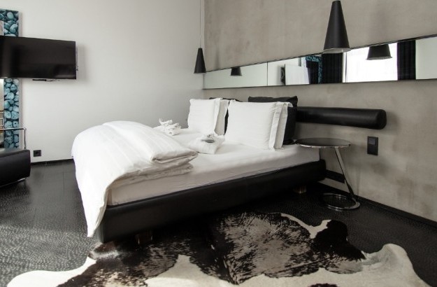 Junior Suite at Thingholt by Center Hotels in Reykjavík with a double bed, concrete feature wall, long mirror, black leather headboard, pendant lights, and a modern lounge chair by a TV.