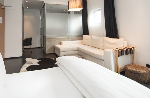Junior Suite at Thingholt by Center Hotels in Reykjavík featuring a white corner sofa, sleek black desk, pendant lighting, cowhide rug, and modern bathroom area with frosted glass partition.