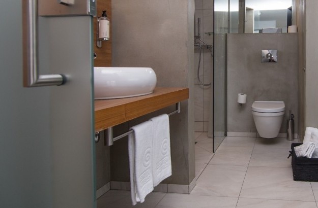 Modern bathroom in the Loft Suite at Thingholt by Center Hotels in Reykjavík featuring a round vessel sink on a wooden counter, walk-in rain shower, wall-mounted toilet, and plush towels in a