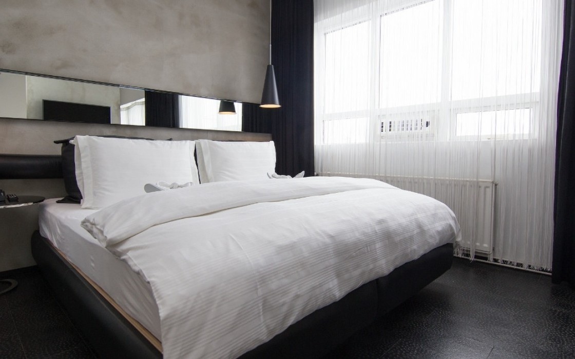 King-size bed in the Loft Suite at Thingholt by Center Hotels in Reykjavík with a concrete feature wall, long mirror panel, black leather headboard, pendant lights, and sheer white curtains