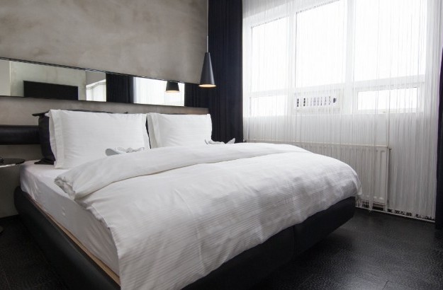 King-size bed in the Loft Suite at Thingholt by Center Hotels in Reykjavík with a concrete feature wall, long mirror panel, black leather headboard, pendant lights, and sheer white curtains