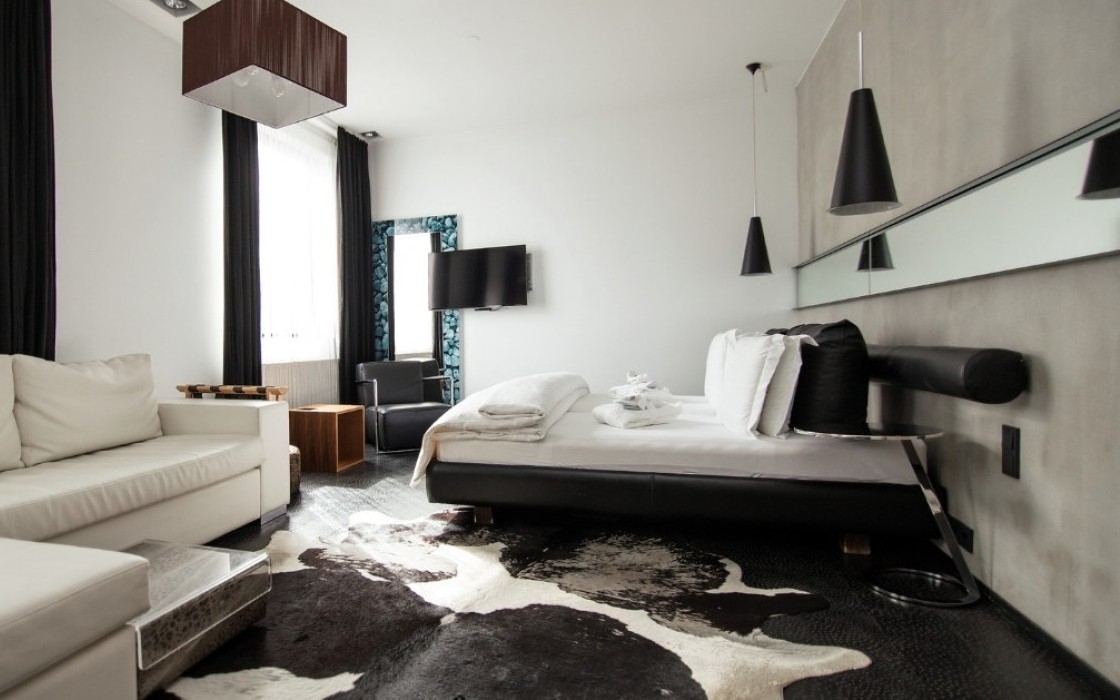 Spacious Junior Suite at Thingholt by Center Hotels in Reykjavík with a white L-shaped sofa, double bed with crisp white linens, mounted TV, cowhide rug, and pendant lighting.