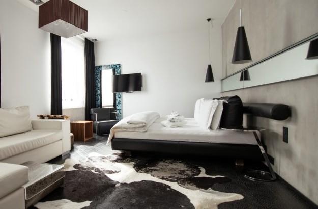 Spacious Junior Suite at Thingholt by Center Hotels in Reykjavík with a white L-shaped sofa, double bed with crisp white linens, mounted TV, cowhide rug, and pendant lighting.