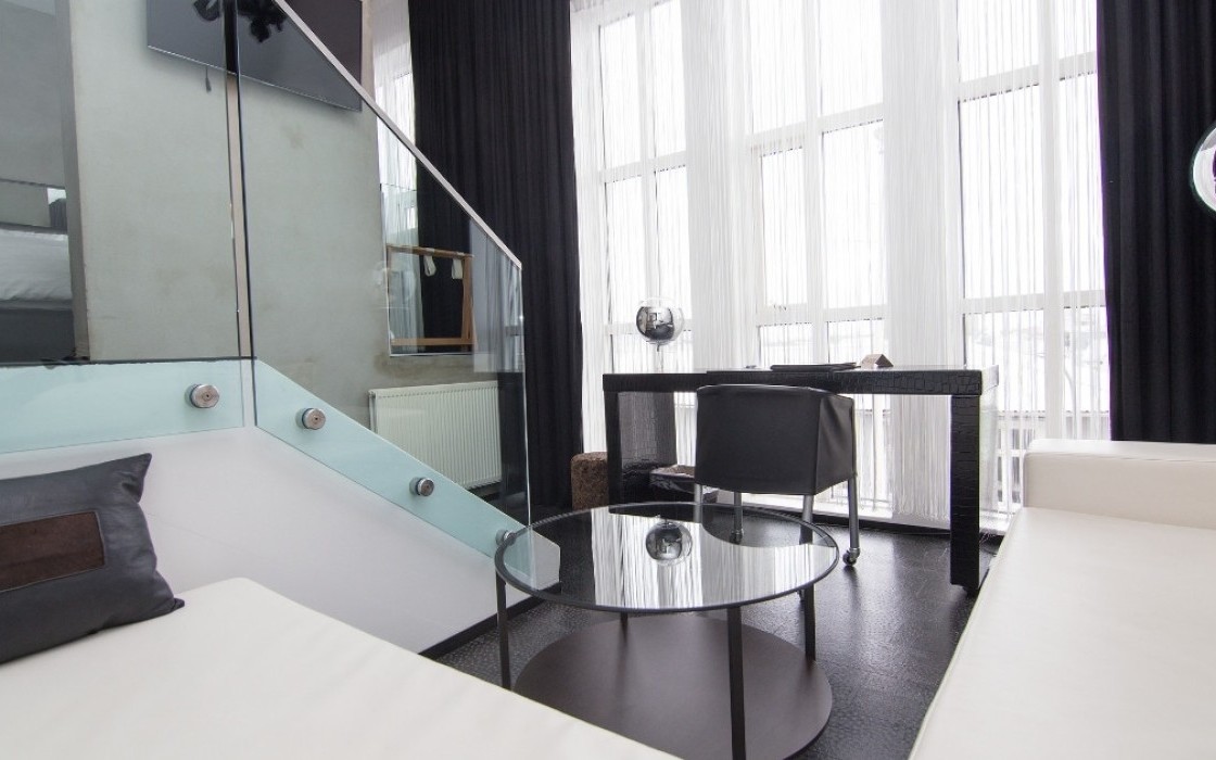 Living area of the Loft Suite at Thingholt by Center Hotels in Reykjavík featuring a white sectional sofa, round glass coffee table, work desk, floor-to-ceiling windows, and black-out curtai