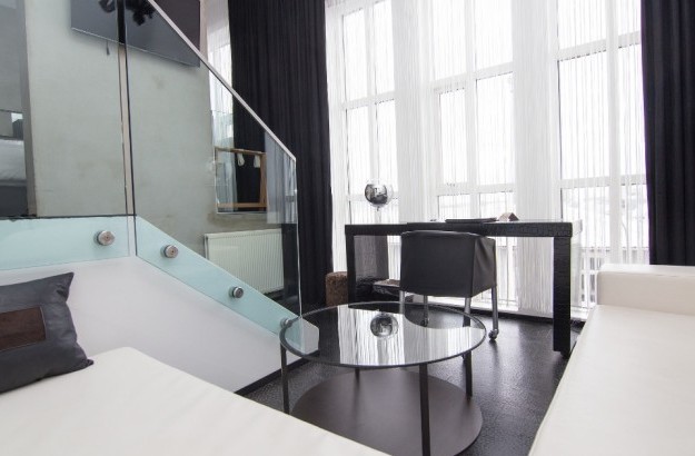 Living area of the Loft Suite at Thingholt by Center Hotels in Reykjavík featuring a white sectional sofa, round glass coffee table, work desk, floor-to-ceiling windows, and black-out curtai