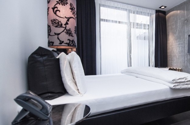 Standard room at Thingholt by Center Hotels in Reykjavik, with white bedding, concrete wall, flat screen TV, large windows with sheer curatins, and a black-floral lamp.