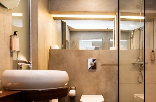 Bathroom in the standard room at Thingholt by Center Hotels in Reykjavik, featuring a round white sink, glass shower, beige stone walls, and backlit mirrors.