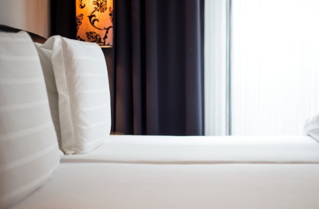 Detail of the bed in the standard room at Thingholt by Center Hotels in Reykjavik, with white-striped pillows, soft linens, blackout curtains, and a decorative floral-patterned lamp.