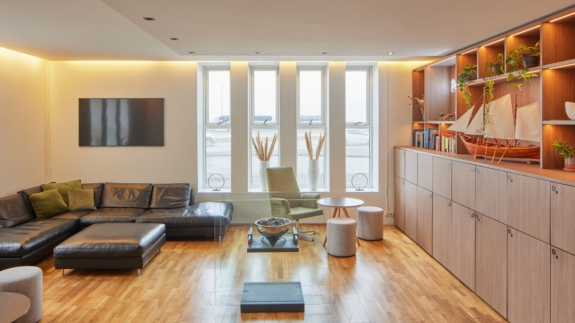 The lobby lounge at Center Hotels Arnarhvoll in Reykjavik with a black leather sofa and wall-mounted TV and a wooden cabinet with decorations.