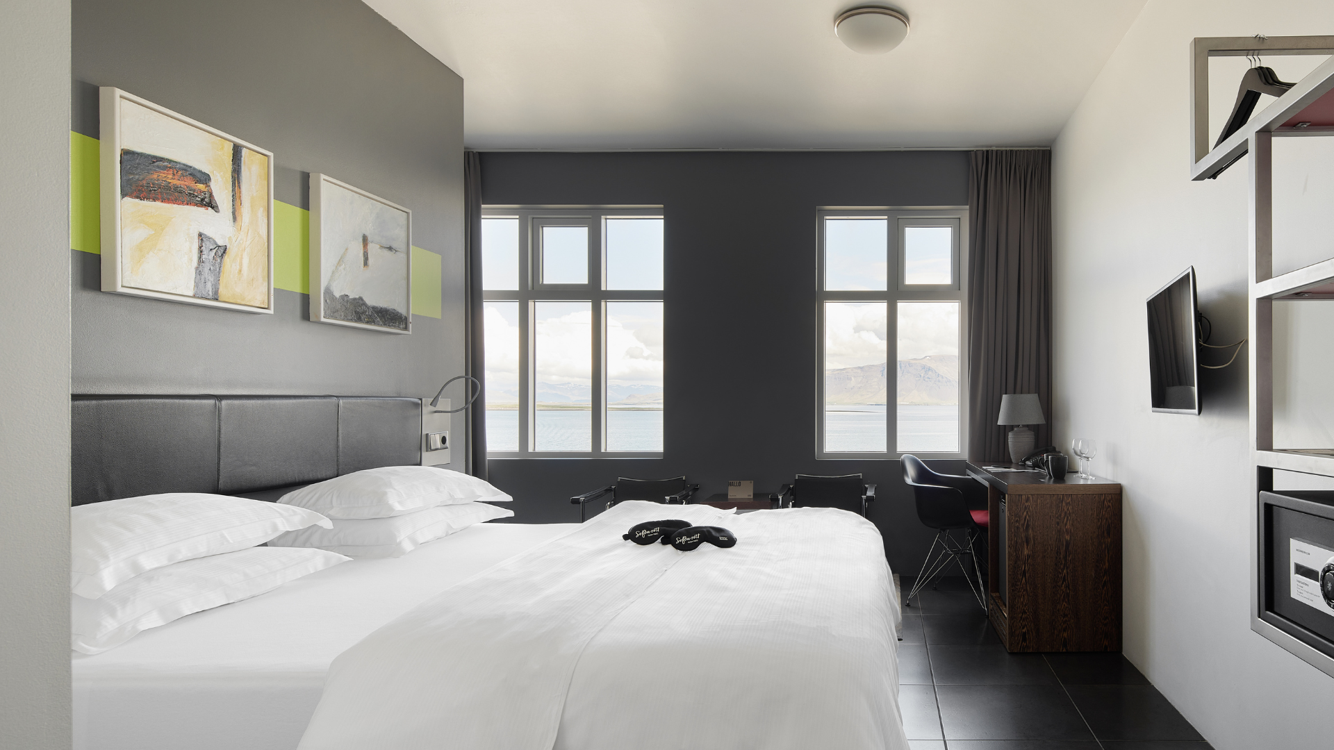 Bright and airy Sea View Room at Center Hotels Arnarhvoll in Reykjavik, featuring a king-size bed, seating area, TV, and panoramic windows offering a scenic ocean and mountain view.