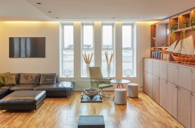 Setustofan í lobby á Center Hotels Arnarhvoll í Reykjavík með svörtum leðursófa, vegghengdu sjónvarpi og viðarskáp með skrauti.