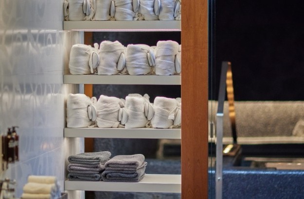 Wellness area at Arnarhvoll with bathrobes and towels in a white and wooden shelf, with the hot tub in the background.