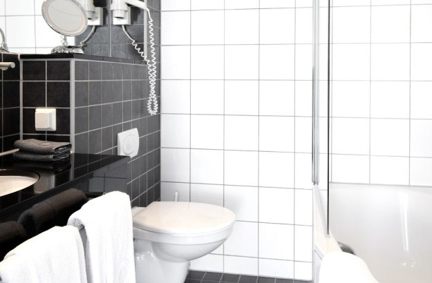 bathroom at Center Hotels Arnarhvoll in Reykjavik with sleek black and white tiles, a bathtub with a glass divider, and a vanity with dark countertop and mounted toiletries.