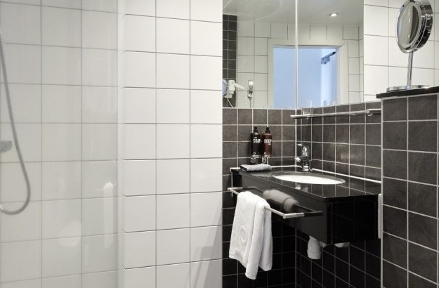 Baðherbergi á Center Hotels Arnarhvoll í Reykjavík, með glersturtu, svörtum vaski og dökkgráum flísalögðum veggjum.