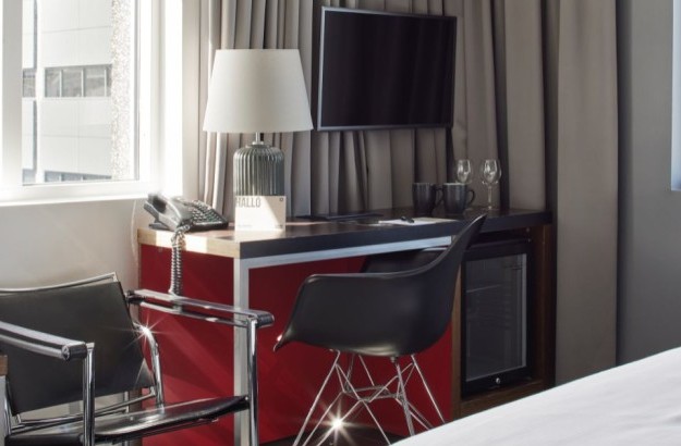 Skrifborðsaðstaða í deluxe herbergi á Center Hotels Arnarhvoli í Reykjavík, með svörtum stólum, flatskjá, lampa, kaffibollum og minibar.