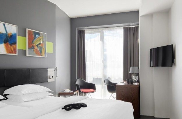 Full view of the Standard Room at Center Hotels Arnarhvoll in Reykjavík with a double bed, colorful abstract wall art, blackout curtains, and a small work area with modern black chairs and so