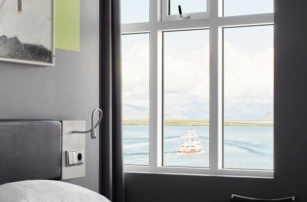 Close-up view from the Sea View Room at Center Hotels Arnarhvoll in Reykjavik, showcasing a large window with a boat sailing on the ocean and mountains in the background.
