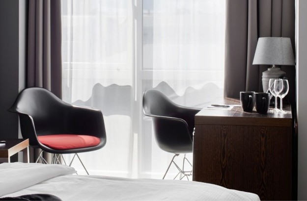 Bright and cozy seating corner in the Standard Room at Center Hotels Arnarhvoll in Reykjavík, featuring two black chairs with red cushions, a wooden desk with mugs and glasses, and natural li