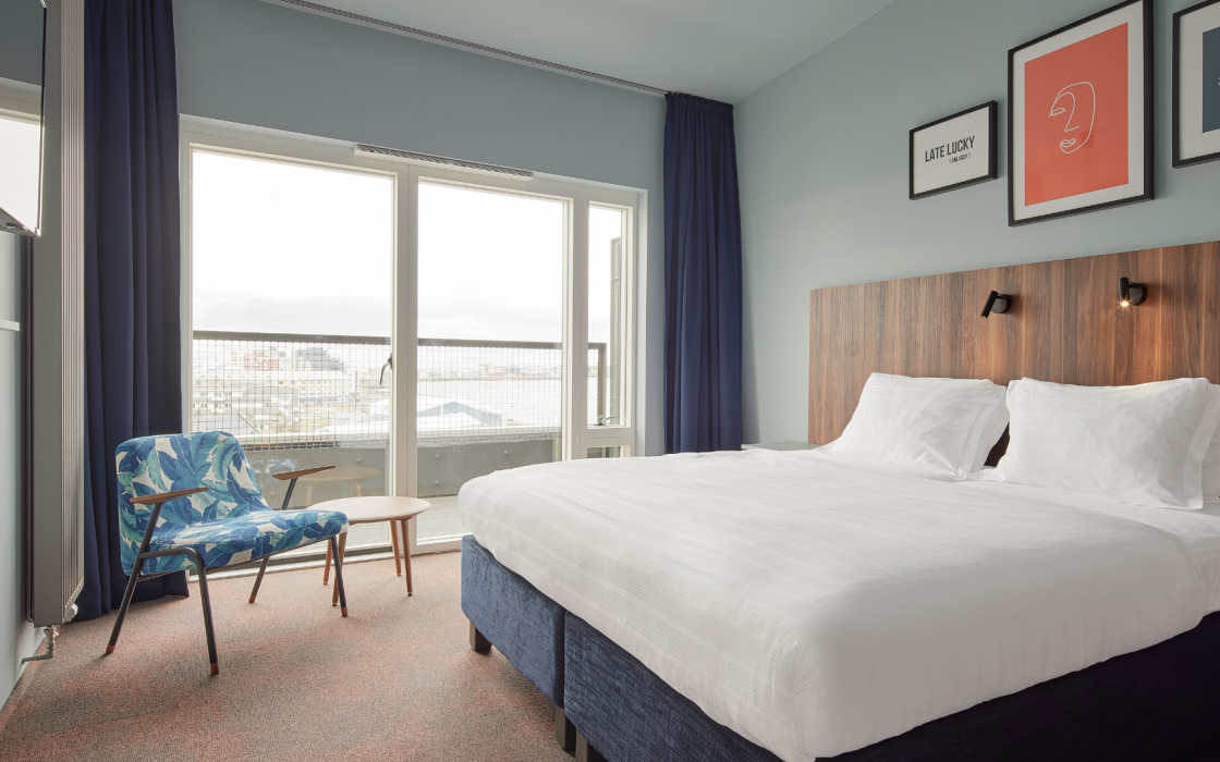 Balcony room at Grandi by Center Hotels in Reykjavik with kind bed, wall art, and large window doors opening to private balcony.