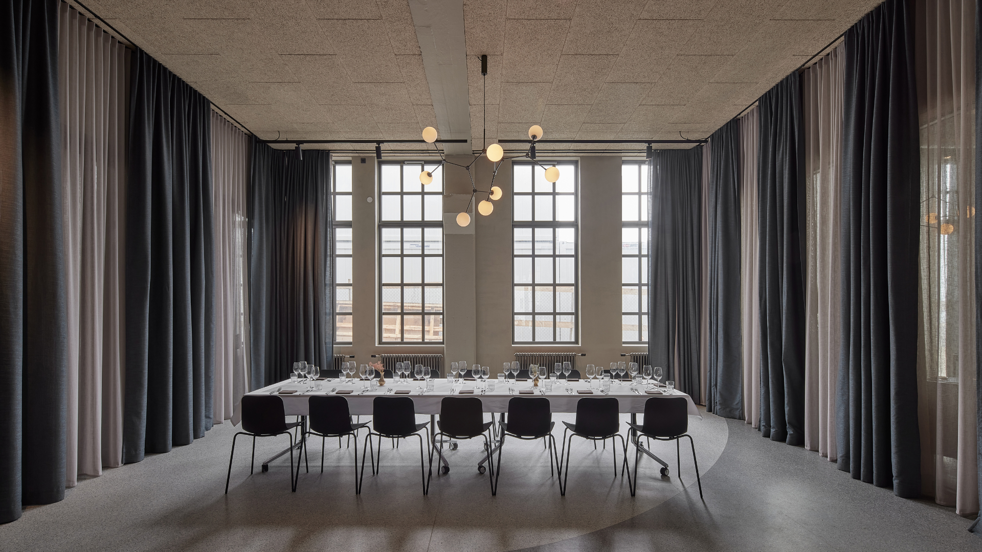 Minimalist conference room at Grandi by Center Hotels in Reykjavik with long meeting table, high arched windows, and blackout curtains for private gatherings.