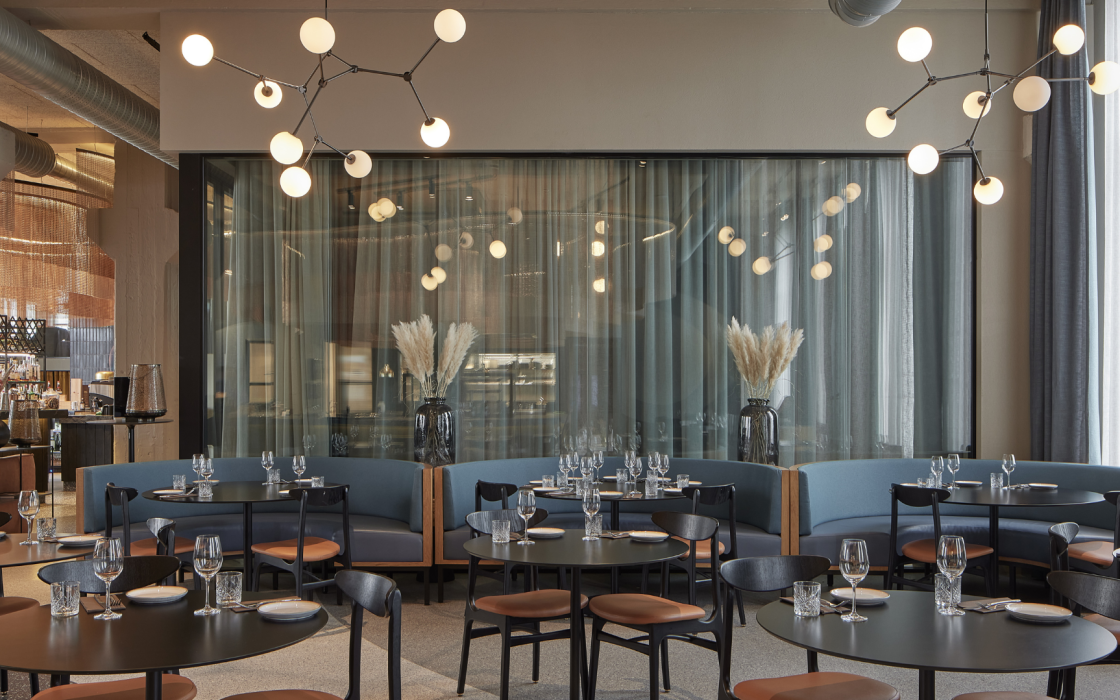 Contemporary restaurant at Grandi by Center Hotels in Reykjavik featuring curved booth seating, minimalist table settings, and striking ceiling lights.