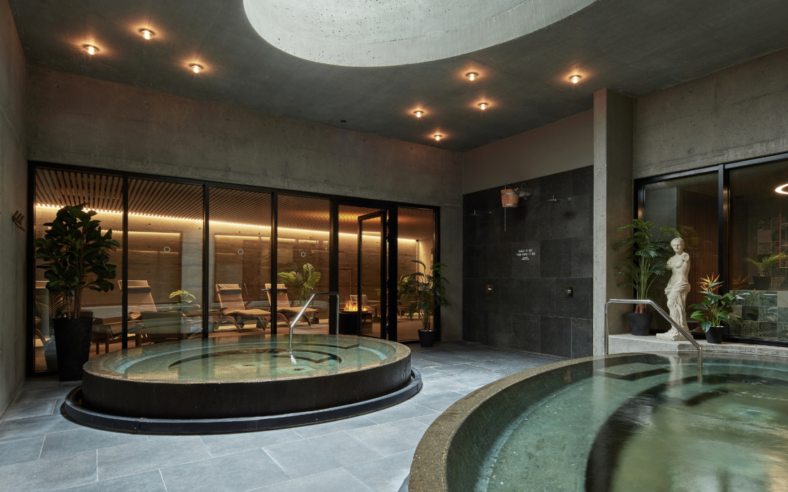 Indoor spa area at Grandi by Center Hotels in Reykjavik with round hot tubs, lounge chairs and natural concrete walls.