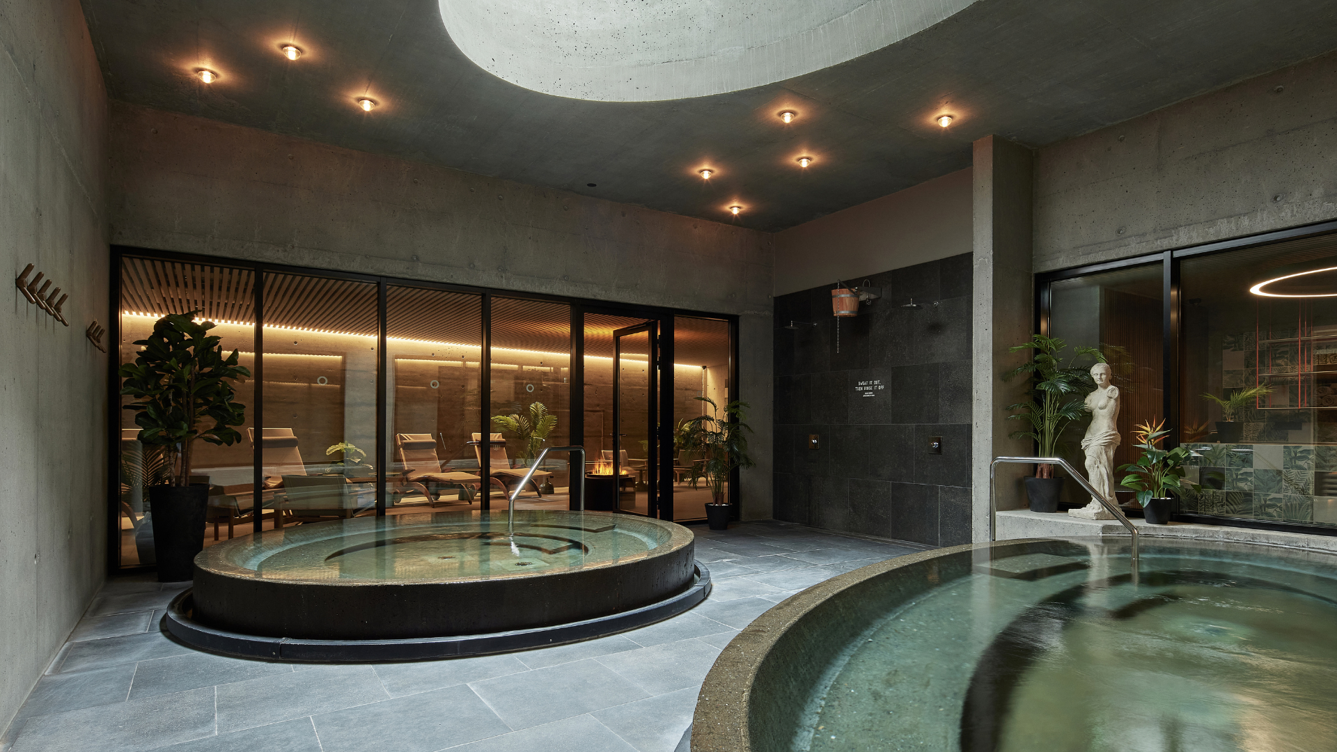 Indoor spa area at Grandi by Center Hotels in Reykjavik with round hot tubs, lounge chairs and natural concrete walls.