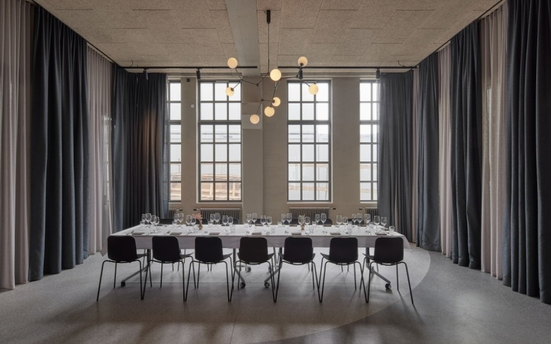 Minimalist conference room at Grandi by Center Hotels in Reykjavik with long meeting table, high arched windows, and blackout curtains for private gatherings.