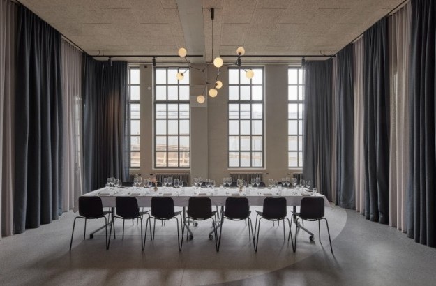 Minimalist conference room at Grandi by Center Hotels in Reykjavik with long meeting table, high arched windows, and blackout curtains for private gatherings.
