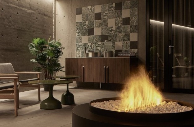 Cozy spa lounge area at Grandi by Center Hotels in Reykjavik, featuring a modern gas fireplace, wood-accented furniture, green tiled wall and indoor plants.