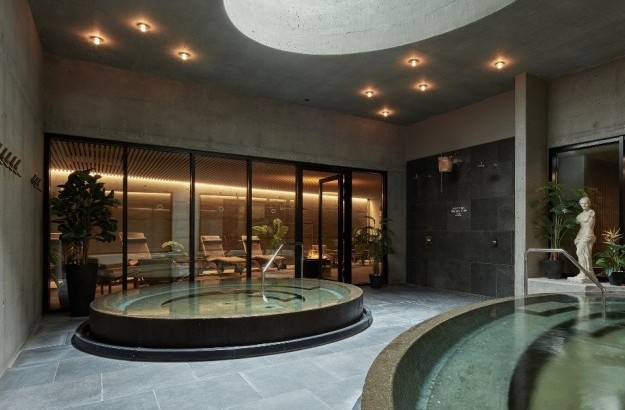 Indoor spa area at Grandi by Center Hotels in Reykjavik with round hot tubs, lounge chairs and natural concrete walls.