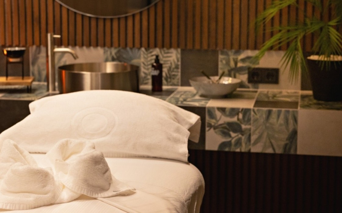 Warmly lit massage room at Grandi spa in Reykjavik, featuring a massage bed with folded towels and a tiled sink area.